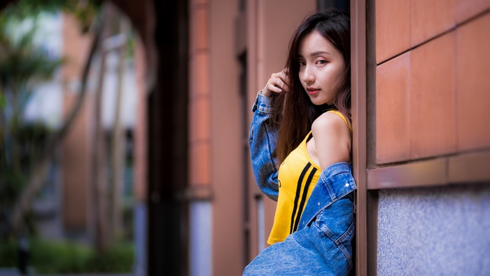 Asian woman with brunette hair wearing a yellow top and denim jacket