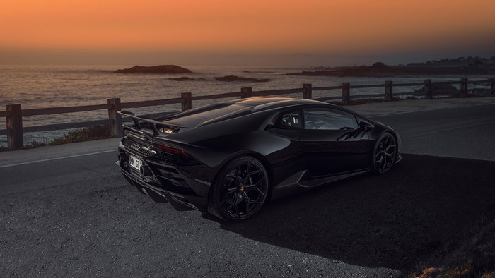 Black Lamborghini Huracán Evo on a coastal road at sunset