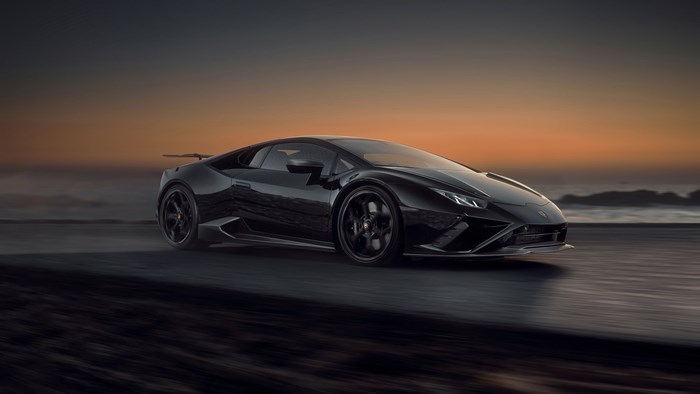 Black Lamborghini Huracan driving on a road at sunset