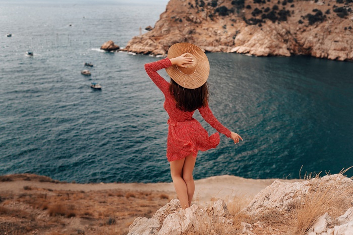 Woman in red dress and hat on cliff overlooking sea