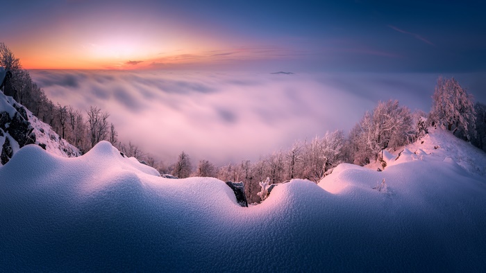 Winter sunrise over foggy mountains with snow-covered trees