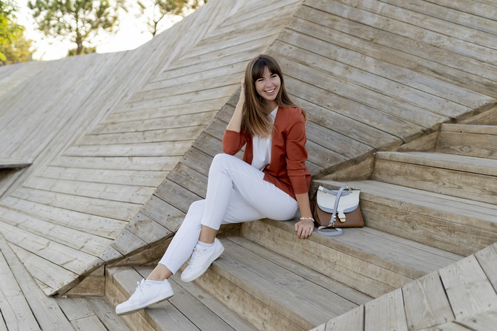 Woman in orange blazer and white pants sitting on wooden stairs