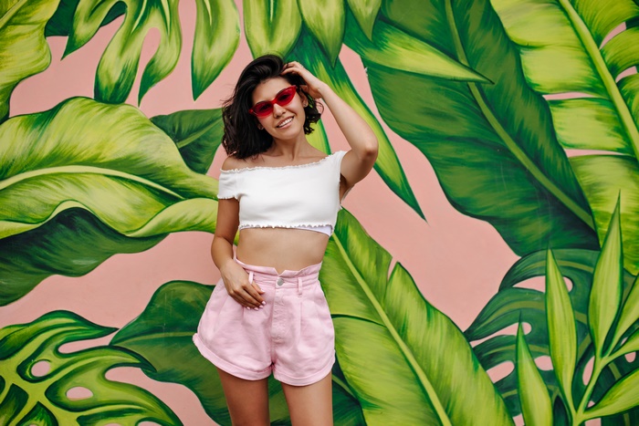Woman in shorts and sunglasses against tropical mural