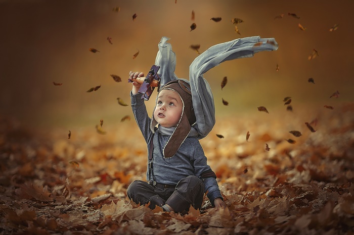 Child in pilot hat with toy airplane in fall leaves