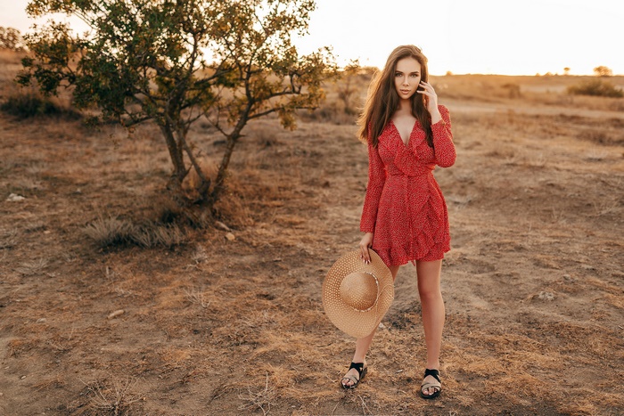 Woman in red dress holding a hat in a field