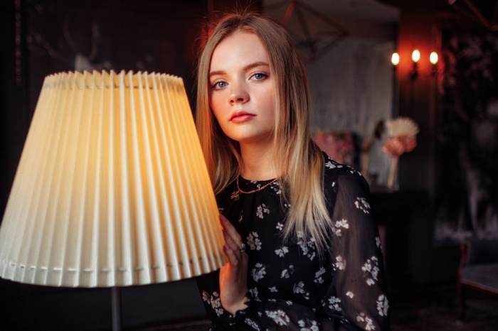 Woman with blonde hair and blue eyes near a lamp