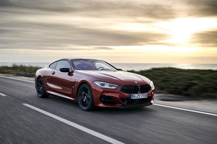 Red BMW 8 Series Coupe driving on coastal road