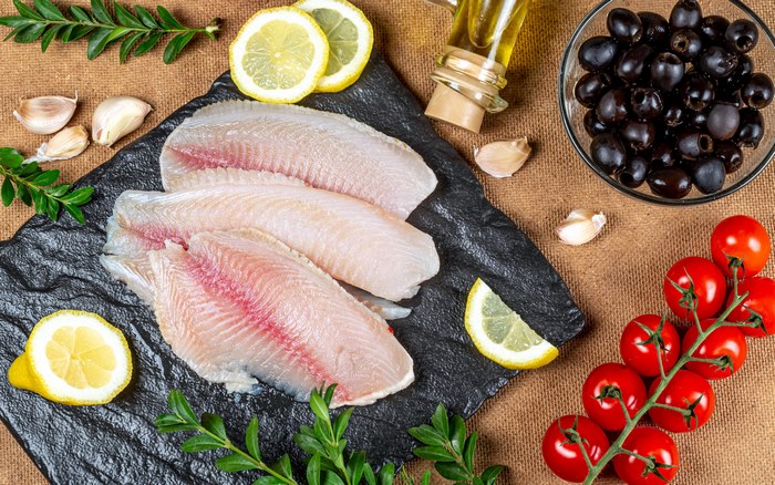 Raw fish fillets with lemons, garlic, tomatoes, olives, and olive oil