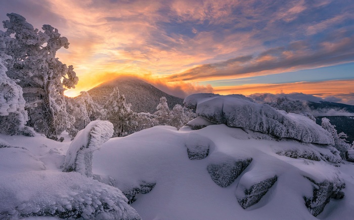 Snow-covered mountain peak at sunset with colorful clouds