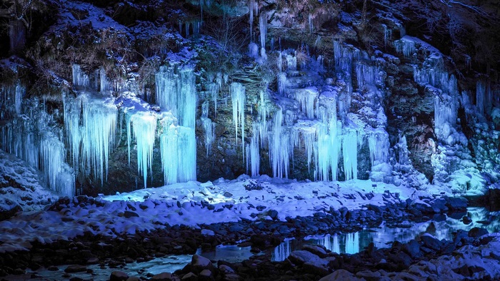Icicles illuminated by blue light on a rocky cliff