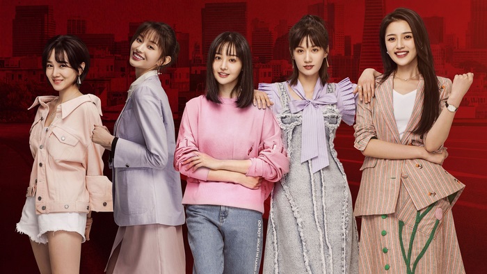 Five young women posing in front of a city skyline