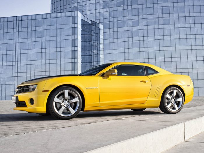 Yellow 2012 Chevrolet Camaro Coupe parked in front of a modern building