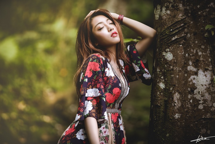 Woman in floral dress leaning against a tree