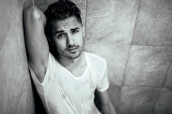 Man in wet white t-shirt leaning against tiled wall