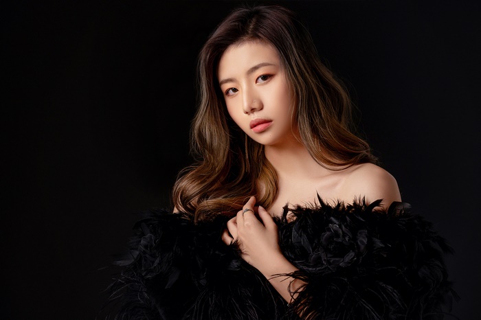Asian woman with brunette hair wearing black feathers