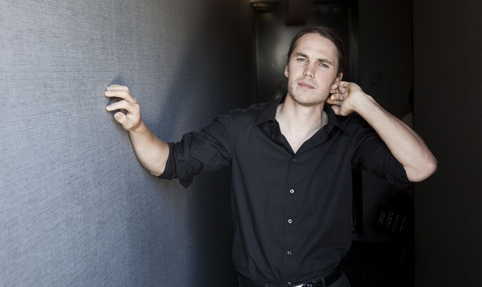 Taylor Kitsch leaning against a textured wall