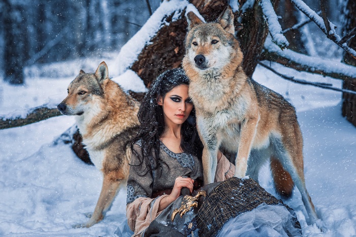 Woman with black hair and two wolves in the snow
