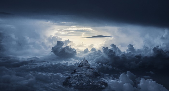 A lone figure stands on a path through clouds