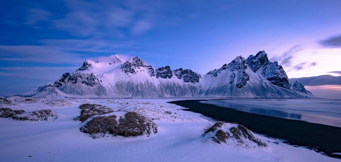 Snowy mountains on a black sand beach at dusk