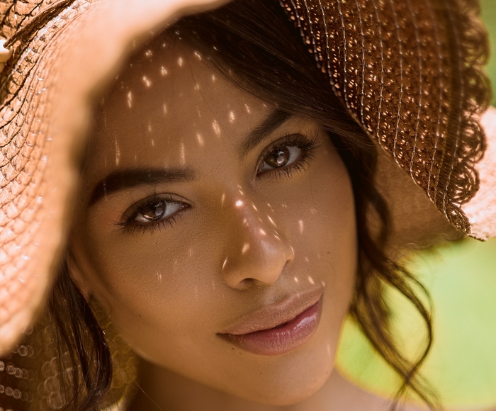 Woman wearing a straw hat with dappled sunlight on her face