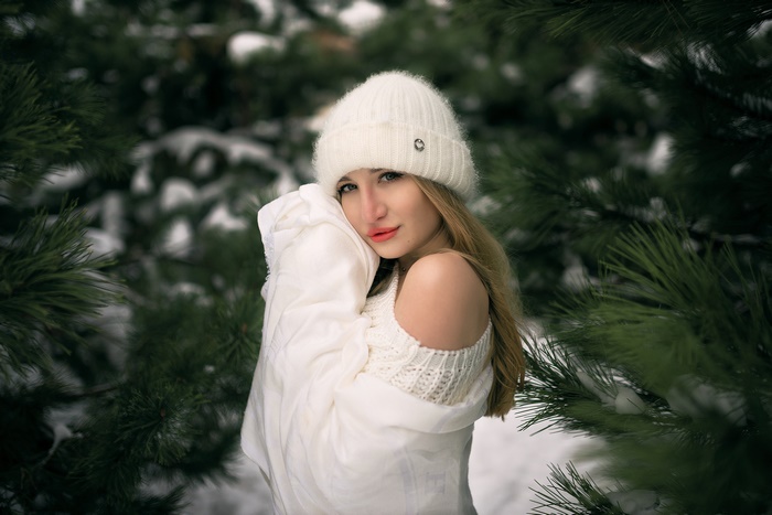Woman in white hat and sweater in snowy forest