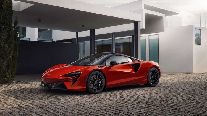 Red McLaren Artura supercar parked in front of a modern house