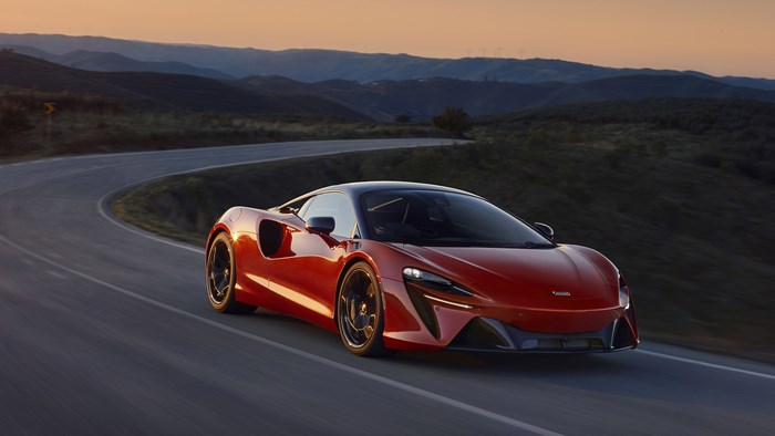 Red McLaren Artura driving on a winding road at sunset