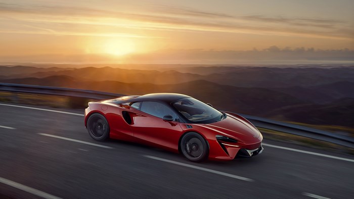 Red McLaren Artura driving on a mountain road at sunset