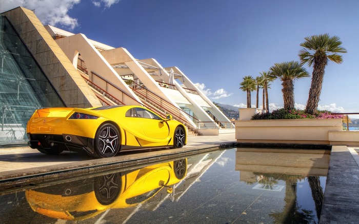 Yellow GTA Spano sport car parked by a modern building