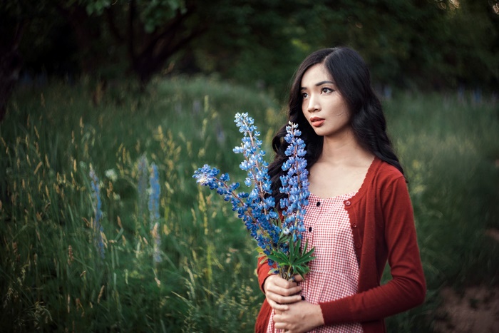 Asian woman holding blue flowers in a field