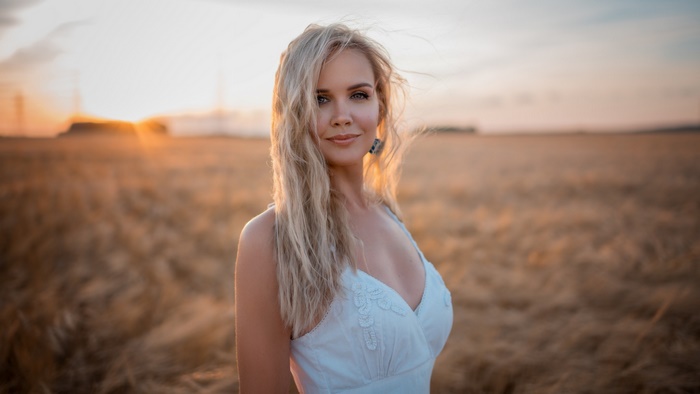 Blonde woman in a white dress in a wheat field at sunset