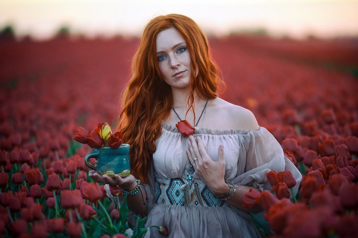 Redhead Woman Among Red Flowers with Blue Eyes