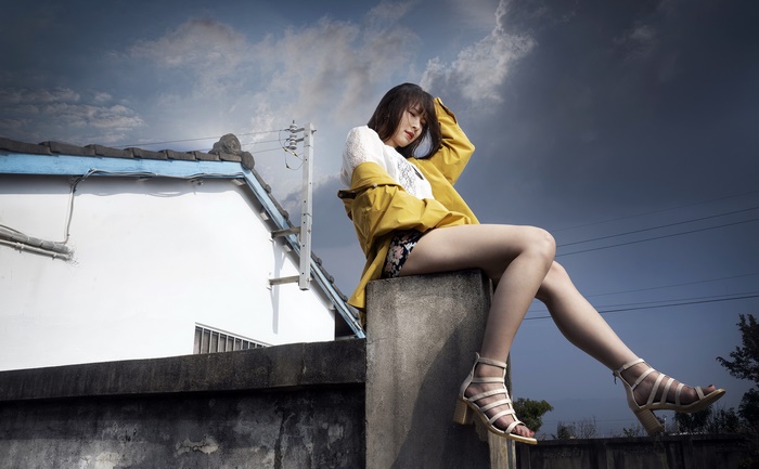 Young Asian woman in yellow jacket sitting on wall