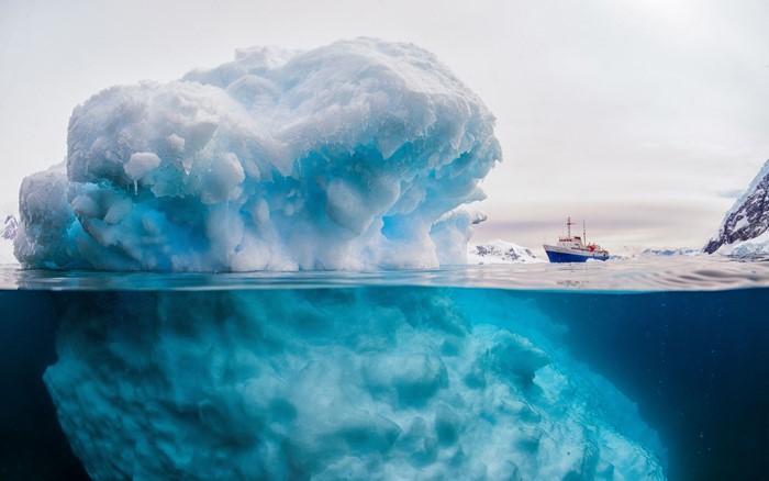 Over and under view of a large iceberg and a ship in the Arctic