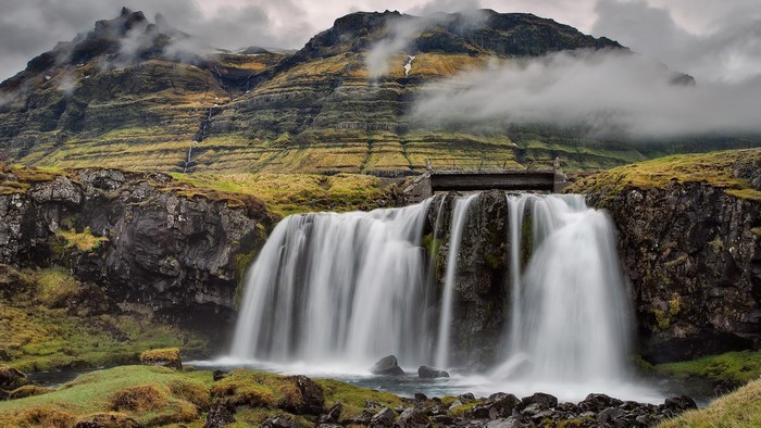 Waterfall cascading down rocky cliffs with mountains in background