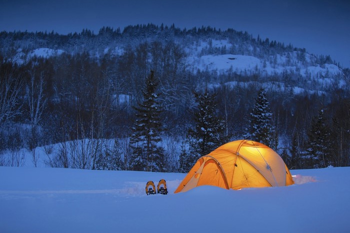 Tent and snowshoes in snowy landscape at dusk