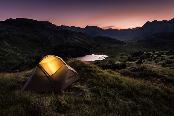Tent glowing in a mountain valley at dusk