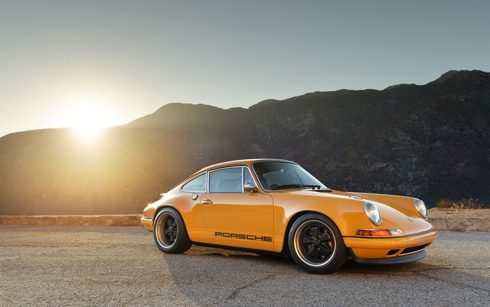 Yellow Porsche 911 parked on a mountain road at sunset