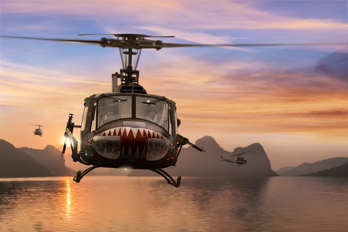 Bell UH-1 Iroquois helicopters flying over water at sunset