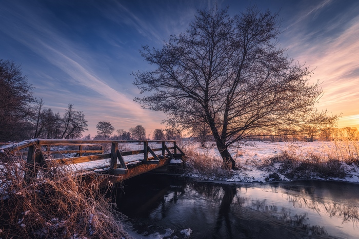 Wooden bridge over a river in winter at sunset
