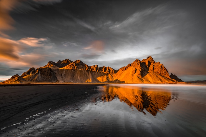 Mountain range reflecting on wet black sand beach at sunset