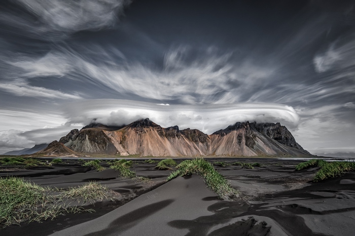 Mountain range with lenticular clouds over black sand beach