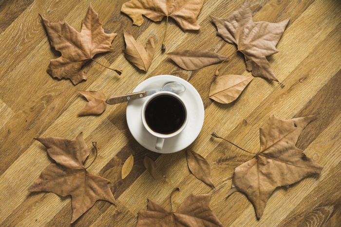 Coffee cup with spoon and dry leaves on wooden table