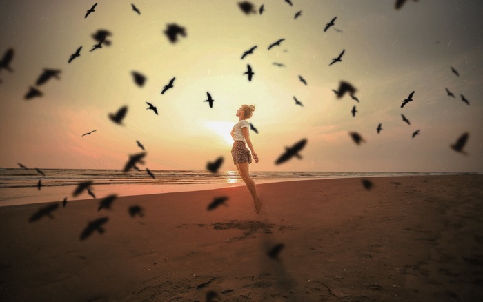 Woman jumping on beach with birds at sunset