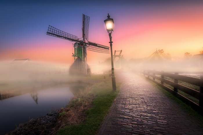 Windmill and street lamp in fog at sunrise