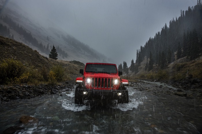 Red Jeep Wrangler driving through a stream in the mountains