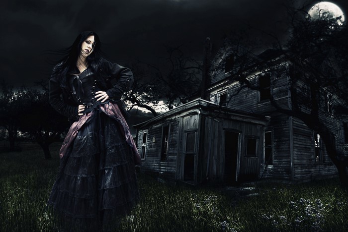 Gothic woman in a dark landscape with a haunted house