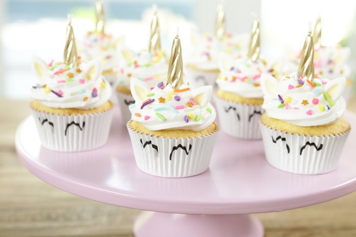 Unicorn cupcakes with candles and sprinkles on a pink cake stand