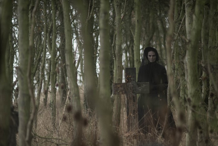 Woman in black veil at a grave in a forest