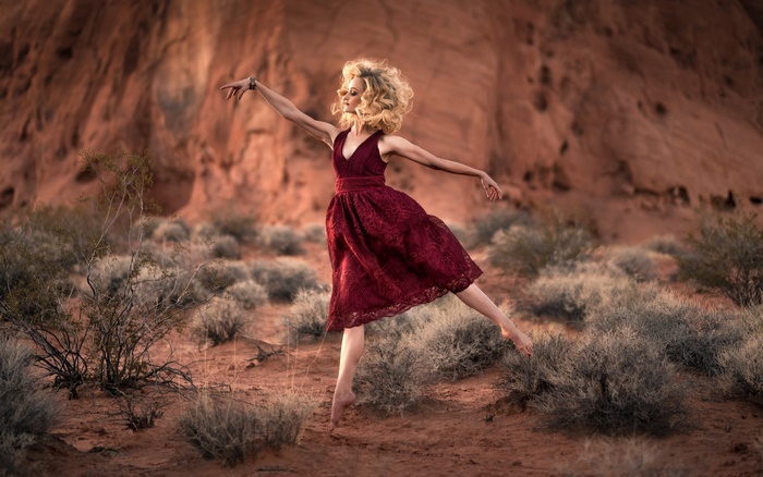 Woman in red dress dancing in desert landscape